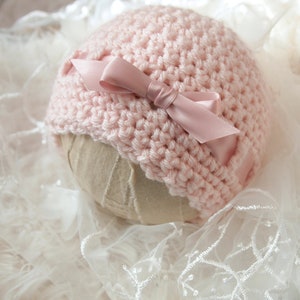 May include: A pink crocheted baby hat with a pink satin bow.