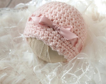 May include: A pink crocheted baby hat with a pink satin bow.