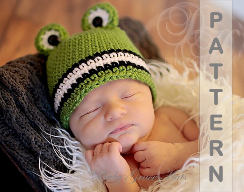 May include: A green crocheted frog hat with black and white stripes and black eyes. The hat is on a baby's head.