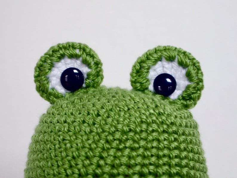 May include: Green crocheted frog hat with white and blue eyes.