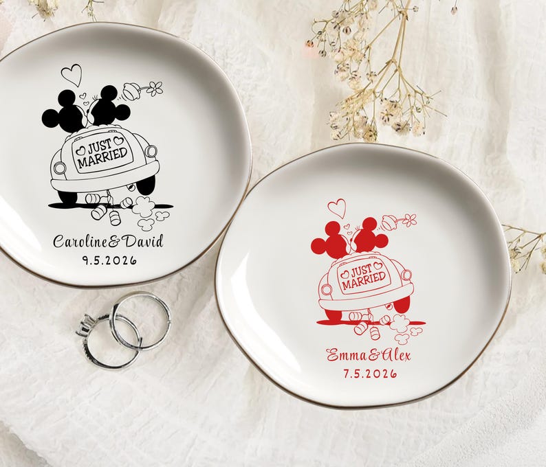 May include: Two white ceramic plates with gold rims. One plate features a black illustration of Mickey and Minnie Mouse in a car with "Just Married" text and the names "Caroline & David" and a date. The other plate has a red illustration with the names "Emma & Alex" and a date.