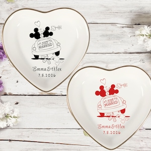 May include: Two heart-shaped trinket dishes with gold rims. One dish features a black illustration of Mickey and Minnie Mouse in a car with "Just Married" text. The other dish has a red illustration. Both dishes have the names "Emma & Alex" and the date "7.5.2026".