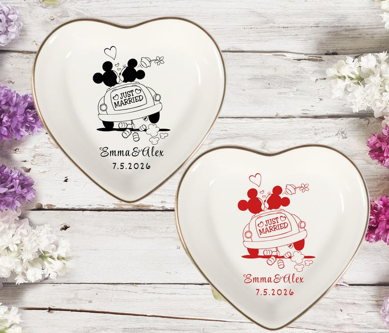May include: Two heart-shaped trinket dishes with gold rims. One dish features a black illustration of Mickey and Minnie Mouse in a car with "Just Married" text. The other dish has a red illustration. Both dishes have the names "Emma & Alex" and the date "7.5.2026".