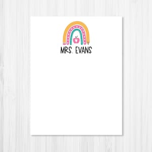 May include: White stationery with a colorful rainbow design and the text "MRS. EVANS" in black. The rainbow features yellow, pink, and teal arches, a pink apple, and a pencil.