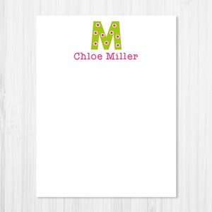 May include: A green letter M with pink polka dots and the name "Chloe Miller" written in pink below it. The letter and name are on a white background.