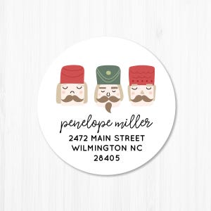 May include: Round white sticker with three nutcracker illustrations. The nutcrackers are wearing red and green hats. The text "penelope miller", "2472 MAIN STREET", "WILMINGTON NC", and "28405" is printed in black.