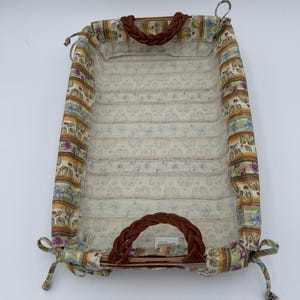 May include: A rectangular basket with a removable fabric liner featuring a floral and striped pattern in shades of green, yellow, and purple. The basket includes two brown braided faux leather handles and fabric ties at each corner for securing.