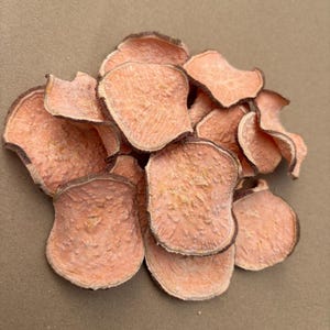 May include: A collection of sweet potato crisps, light orange in colour with a darker brown edge. The crisps have a textured surface and are arranged on a light brown surface.