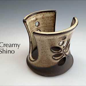 May include: Creamy white ceramic utensil holder with a brown glaze and a cut-out design of leaves. The holder is designed to hold utensils upright.