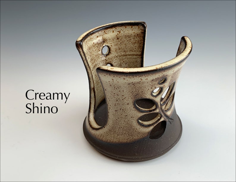 May include: Creamy white ceramic utensil holder with a brown glaze and a cut-out design of leaves. The holder is designed to hold utensils upright.
