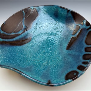 Puede incluir: Un plato de servir de cerámica con un esmalte azul y negro. El plato tiene un borde ondulado y un diseño único.