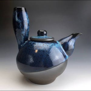 以下が含まれることがあります： ユニークな注ぎ口と蓋が付いた青と茶色のセラミック製のティーポット。ティーポットは斑点のある釉薬が施されています。
