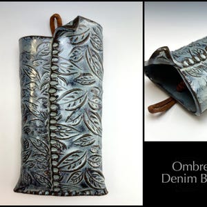 May include: A ceramic wall vase with a blue and white ombre glaze and a leaf pattern. The vase has a brown leather strap for hanging.