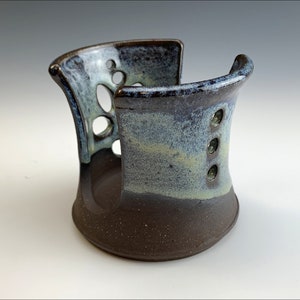 May include: A ceramic soap dish with a brown glaze and a light blue and white glaze. The dish has a unique design with cutouts and holes.