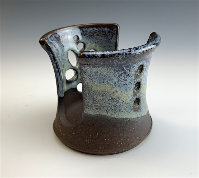 May include: A ceramic soap dish with a brown glaze and a light blue and white glaze. The dish has a unique design with cutouts and holes.