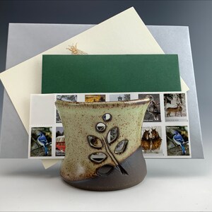 May include: A ceramic holder with a leafy design and a speckled glaze. The holder is brown and green and has a cutout design. The holder is sitting on a stack of envelopes with stamps.