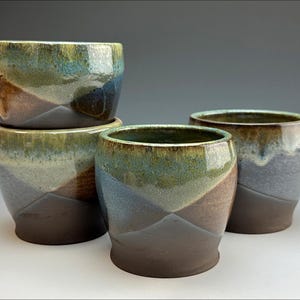 May include: Four ceramic cups with a blue, green and brown glaze. The cups are stacked in a pyramid shape.
