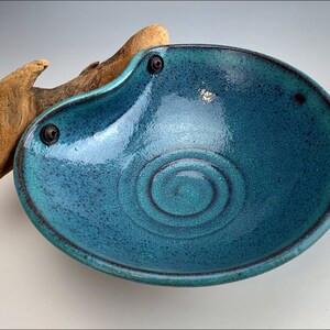Può includere: Una ciotola in ceramica blu turchese con un bordo marrone scuro e un design a spirale al centro. La ciotola è fissata a un pezzo di legno di deriva con due rivetti metallici.