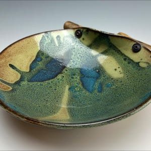 Può includere: Un piatto in ceramica con una glassa verde, blu e marrone. Il piatto ha un manico in legno con dettagli in metallo.