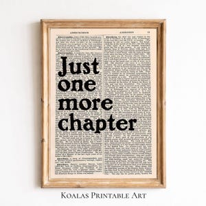 May include: A framed print featuring a vintage dictionary page with the words "Just one more chapter" in bold black letters. The print has a wooden frame and is labeled "Koalas Printable Art" at the bottom.