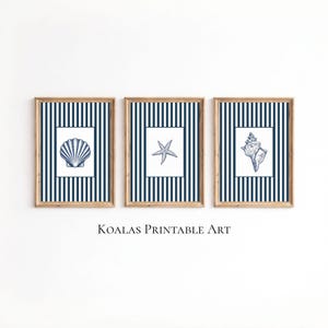 May include: Three framed prints with nautical themes. Each print has a wooden frame and a white background with a blue and white striped border. The prints depict a seashell, a starfish, and a conch shell. The text "KOALAS PRINTABLE ART" is below the prints.