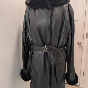May include: A black leather coat with a hood and a belt. The coat has a faux fur lining on the hood and cuffs. The belt has a silver buckle. The coat is displayed on a mannequin.