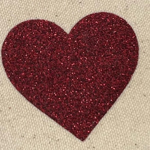 May include: A large, heart-shaped appliqué with a sparkling, deep red glitter finish. The heart is centered on a neutral-toned, textured fabric, creating a striking contrast. Ideal for crafting or decorative projects.