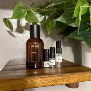 May include: A white ceramic mug with a black handle and the text "But First, Coffee" in a bold, black font. The mug is set against a blurred background, suggesting a cozy setting. The mug appears to be approximately 4 inches tall.