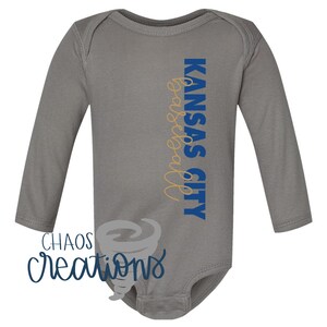 May include: Grey long-sleeved baby onesie with the text "KANSAS CITY basketball" in blue and gold lettering.