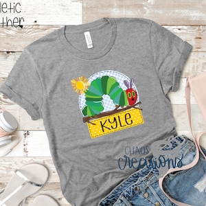 May include: Grey t-shirt featuring a colourful caterpillar graphic and the name "Kyle" on a yellow banner. The caterpillar is on a branch with a sun behind it. The shirt is made of athletic heather fabric.