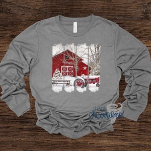 May include: A long-sleeve gray shirt featuring a winter scene with a red barn, tractor, and Christmas tree. The graphic includes a star and snow. The text "Chaos Creations" is visible.