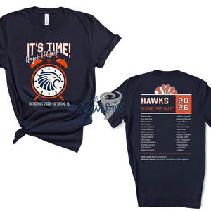 May include: Navy blue t-shirt with the text "IT'S TIME! Hawk O'Clock" and a graphic of an alarm clock with a hawk emblem. The shirt also has "Nationals 2026 - Orlando, FL" printed on it. The back of the shirt has "HAWKS Olathe East Cheer 2026" and a list of names.