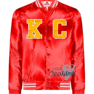 Puede incluir: Chaqueta bomber de sat&eacute;n rojo con pu&ntilde;os y cuello a rayas blancas y rojas. La chaqueta presenta una gran "KC" amarilla en la parte delantera.