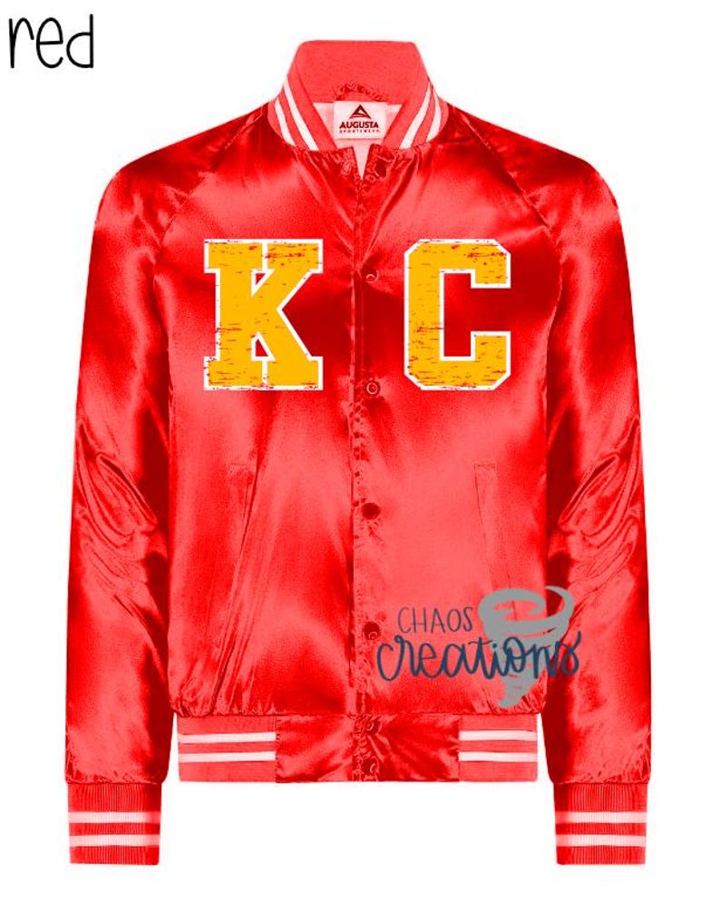 Puede incluir: Chaqueta bomber de sat&eacute;n rojo con pu&ntilde;os y cuello a rayas blancas y rojas. La chaqueta presenta una gran "KC" amarilla en la parte delantera.