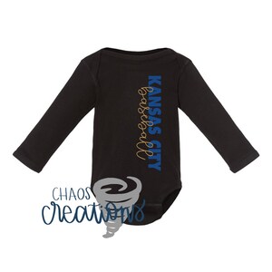 May include: Black long-sleeved baby onesie with the text "Kansas City Basketball" in blue and gold lettering.
