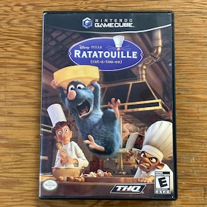 Könnte beinhalten: Eine Nintendo GameCube Videospielhülle für das Spiel Ratatouille von Disney Pixar. Das Cover zeigt eine blaue Ratte mit einer gelben Schüssel, einen Koch mit weißer Mütze und den Titel Ratatouille mit der Aussprache rat-a-too-ee in Weiß.