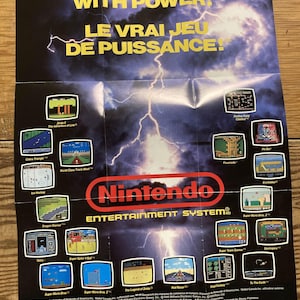 May include: A vintage Nintendo Entertainment System poster with a dark blue and yellow color scheme. The poster features the text "NOW YOU'RE PLAYING WITH POWER!" and "LE VRAI JEU DE PUISSANCE!" along with various game screenshots, including Super Mario Bros. and The Legend of Zelda.