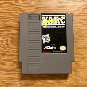 May include: A gray Nintendo Entertainment System (NES) game cartridge for the game NARC. The cartridge has a black label with white and yellow text, including "NO ONE HAD THE GUTS... UNTIL NOW" and "Just say no."