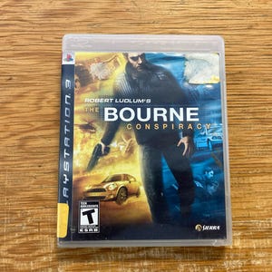 May include: The Bourne Conspiracy PlayStation 3 game case. The cover features a man holding a gun, with the title "The Bourne Conspiracy" and a car and helicopter in the background. The game is rated T for Teen.