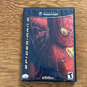 May include: A Nintendo GameCube video game case for Spider-Man 2. The cover features a red and blue Spider-Man mask with a web pattern, the title Spider-Man 2 in yellow text, the Activision logo, and a black T for Teen ESRB rating symbol.