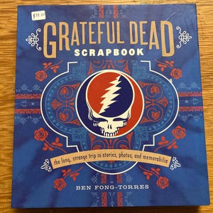 May include: A blue Grateful Dead scrapbook with the band's logo, a skull with a lightning bolt, in the center. The cover features the text "GRATEFUL DEAD SCRAPBOOK" and "the long, strange trip in stories, photos, and memorabilia."