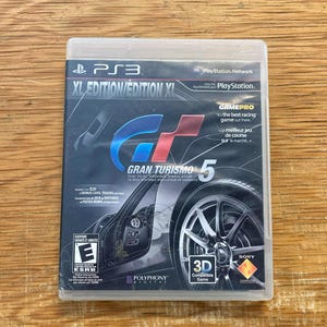 May include: Gran Turismo 5 XL Edition video game for the PlayStation 3 console. The game case features a dark background with a car graphic and the game's logo in red and blue. Includes bonus cars and tracks.