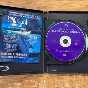 May include: An open black DVD case with a purple disc featuring "The Tale of the Princess Kaguya." The left side displays promotional material for "Song of the Sea" in blue and white, with text in English and French.