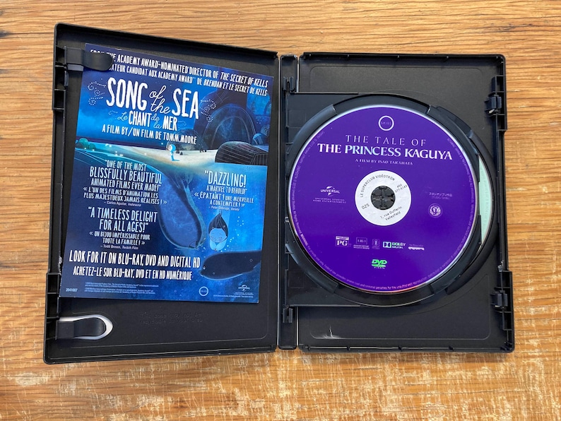 May include: An open black DVD case with a purple disc featuring "The Tale of the Princess Kaguya." The left side displays promotional material for "Song of the Sea" in blue and white, with text in English and French.