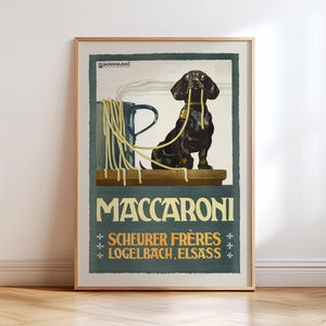 以下が含まれることがあります： 黒いダックスフント犬がスパゲッティを口にくわえた、額入りのヴィンテージポスター。ポスターは青とベージュの配色で、大きな文字で「Maccaroni」と書かれています。「Scheurer Frères Logelbach, Elsass」の文字も含まれています。