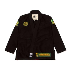 May include: Black Jiu-Jitsu uniform with green and yellow patches and logos. The uniform has a collar and long sleeves. The brand name "SHOYOROLL" is visible on the patches and labels. The uniform is designed for martial arts training and competition.