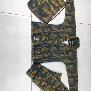 Könnte beinhalten: Kampfkunst-Uniform-Set mit Tarnmuster, bestehend aus Jacke, Hose und Kordelzugbeutel. Der Stoff weist eine Mischung aus Grün-, Braun- und Schwarztönen auf. Jacke und Hose haben Aufnäher mit Text und Logos. Der Kordelzugbeutel trägt den Text "RVCA".