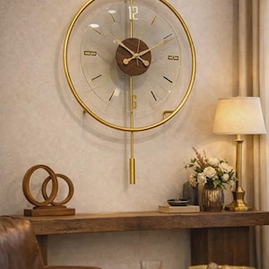 Könnte beinhalten: Eine goldfarbene, runde Wanduhr mit einem klaren Glaszifferblatt und einem hölzernen Mittelteil. Die Uhr hat goldene Zeiger und ein Pendel. Die Uhr ist an einer hellen Wand befestigt. Teil eines Einrichtungs-Themas.