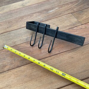 May include: Black metal rack with three hooks, measuring 11 inches long, on a wooden surface.