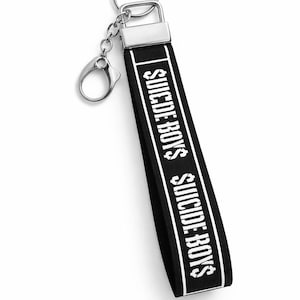 May include: Black keychain wrist strap with the text "SUICIDE BOYS" in white. The strap has a silver metal clasp and key ring. The design is simple and bold, with a clear, readable font.